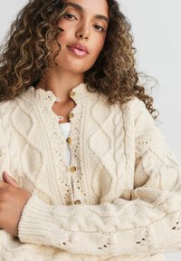 Cremefarvet strikket cardigan med diamantmønster, ribbede manchetter og træknapper. Struktureret stof med et hyggeligt udseende.