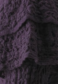 Lila texturerad tyg med lager av kanter, med ett upphöjt mönster. Det mjuka materialet verkar fluffigt och lätt.