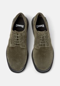 Scarpe in suede verde oliva con suole e lacci in gomma nera, con il logo "CAMPER" visibile sulle sole.