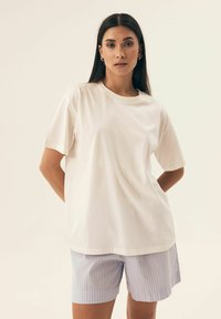 Biała bawełniana koszulka z krótkim rękawem i okrągłym dekoltem, w połączeniu z jasnoniebieskimi szortami w paski. Gładka tekstura, luźny krój.