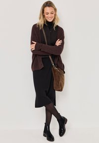 Cárdigan burdeos sobre un cuello de cisne negro, combinado con una falda negra, medias negras y botines negros brillantes. Bolso de hombro marrón.