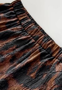 Spódnica z marszczeniami wykonana z pomarszczonego materiału w odcieniach czerni i brązu, z elastycznym pasem i teksturowaną powierzchnią.