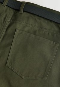 Olivově zelené kalhoty s hladkým, texturovaným povrchem. Mají jednu zadní kapsu obdélníkového tvaru s prošitým detailem. Černý pás.