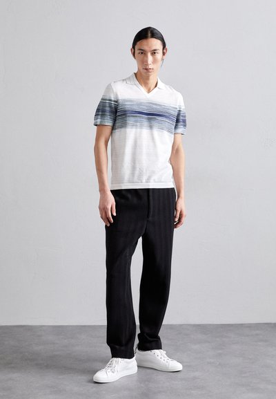 Πόλο μπλούζα με κοντό μανίκι σε λευκό χρώμα με μπλε οριζόντιες ρίγες, συνδυασμένη με μαύρο παντελόνι με μοτίβο και λευκά αθλητικά παπούτσια. Απλός, casual σχεδιασμός.