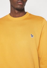 Suéter amarillo con cuello redondo, textura de canalé y un pequeño bordado de cebra multicolor en la zona izquierda del pecho.