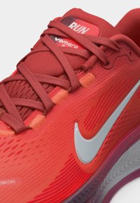 Gros plan sur une chaussure de course Nike rouge avec les lacets attachés, affichant l'étiquette "Run" et le logo blanc Nike swoosh sur la tige texturée.