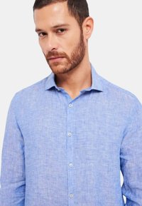 Camicia button-up in lino azzurro chiaro con colletto classico e una texture sottile, dotata di patta frontale con bottoni a lunghezza completa e maniche lunghe.