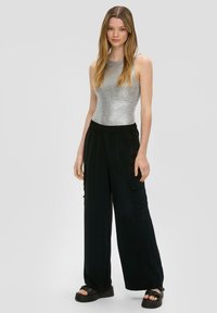 Šedý žebrovaný top bez rukávů spárovaný s volnějšími černými cargo kalhotami s kapsami. Model nosí robustní černé sandály. Jednoduchý a neformální outfit.