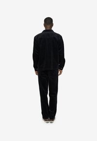 Black corduroy jacket and pants set, featuring a relaxed fit, textured surface, and button accents, viewed from the back.