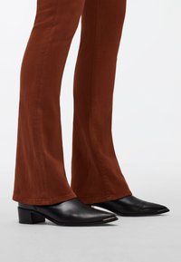 Pantalons évasés marron associés à des talons aiguille noirs avec un gros talon bloc et des accents en argent près de la pointe.