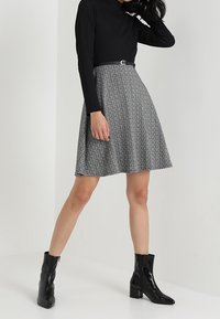 Svart långärmad topp i kombination med en knälång, utsvängd kjol med grått mönster, accentuerad med ett smalt bälte och glänsande svarta anklarboots.