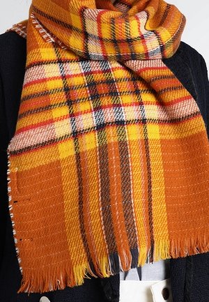 Écharpe épaisse tissée avec un motif à carreaux orange, jaune, rouge et noir enroulée autour du cou et des épaules d'une personne.