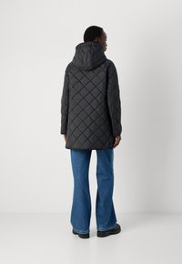 Svart quiltet pufferjakke med hette, med et diamantmønster, kombinert med blå vide jeans og robuste svarte støvler.