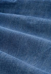 Denimstof in diepblauw, getextureerd met subtiele keperweving, met vouwen en plooien die wijzen op de zachte val.