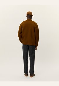 Brown knit sweater with a relaxed fit, grey tailored trousers, and a brown cap. Smooth texture and minimalistic design.