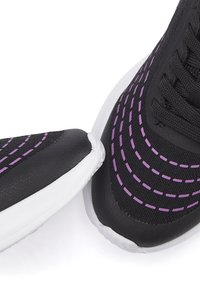 Schwarze Sportschuhe mit einer strukturierten Oberseite, die lila gestickte Details aufweist. Weiße Gummisohlen, abgerundete Zehen und Schnürsystem.