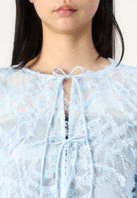 Light blue sheer top with a textured, frayed design. It features a tied closure at the neck and a soft, flowing look.