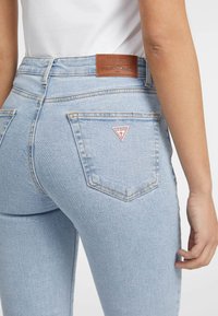 Ljusblå denimjeans med en smal passform. Funktioner inkluderar en triangulär röd logotyp på bakfickan och en brun läderetikett vid midjan.