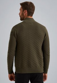 Maglione lavorato a maglia verde oliva con un motivo a diamante testurizzato, colletto e orlo a coste, dotato di una toppa decorativa sulla parte superiore del braccio.