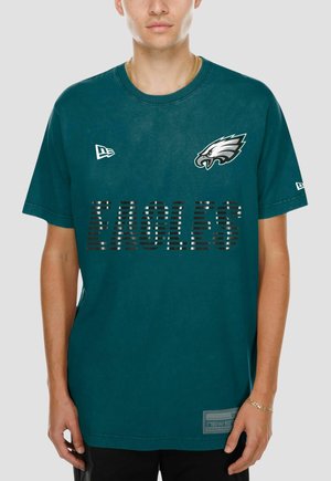 Uomo che indossa una maglietta verde scuro Philadelphia Eagles con il logo della squadra sul petto sinistro e testo a strisce ""EAGLES"" sul davanti.