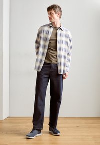 Casual outfit featuring a light plaid shirt with blue and cream stripes, olive green t-shirt, dark blue jeans, and gray sneakers.