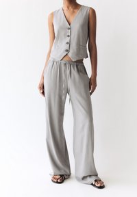 Gilet en lin gris croppé avec cinq boutons associé à un pantalon ample à taille élastique et à cordon. La texture est douce ; le tissu semble léger.