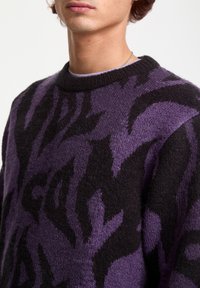 Suéter de patrón morado y negro, hecho de material de punto suave, con diseño de cuello redondo y acentos texturizados a lo largo.