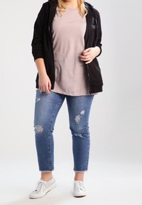 Felpa nera, t-shirt rosa chiaro, jeans blu strappati e sneakers bianche. Tessuti morbidi, design casual e dettagli con orlo sfilacciato.