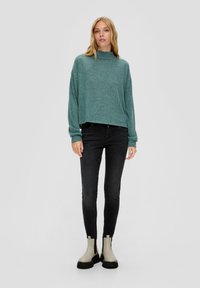 Turkusowy, krótki sweatshirt z wysokim kołnierzem i długimi rękawami, połączony z czarnymi dopasowanymi dżinsami oraz beżowymi botkami na kostkę z grubą podeszwą.