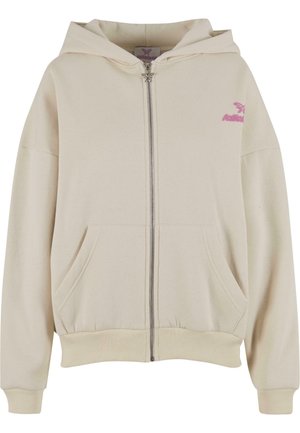 Cream zip-up hoodie with a large front pocket and ribbed cuffs. Features a pink logo on the left chest and a spacious hood. Soft texture.