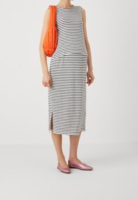 Pruhované černo-bílé midi šaty se bočním rozparkem, doplněné o prošívanou oranžovou kabelku přes rameno a lesklé růžové baleríny.