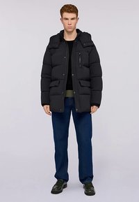 Černá péřová bunda s kapucí, zdobená prošívanými částmi, zipovou kapsou na hrudi a dvěma předními kapsami, v kombinaci s modrými džínami.