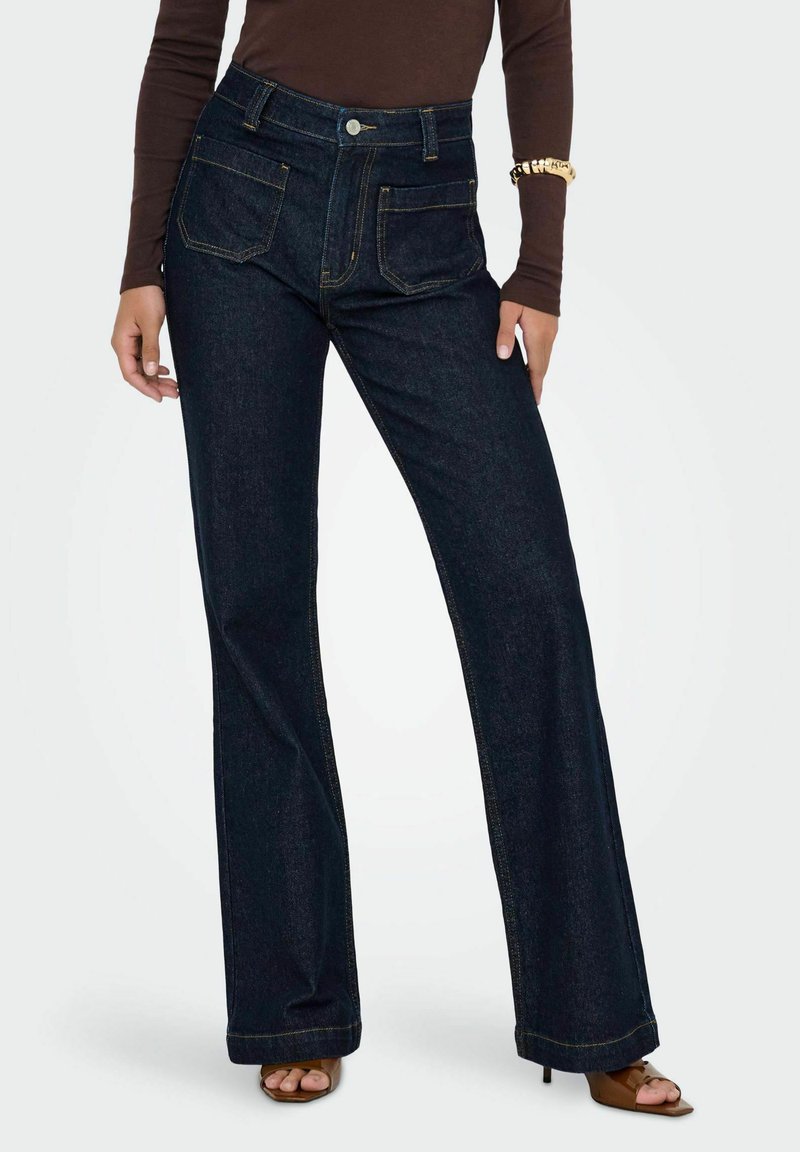 Jean flare en denim bleu foncé avec taille haute, présentant des poches avant et arrière, des coutures jaunes et une fermeture à bouton minimaliste.