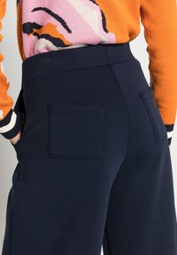 Granatowe spodnie o dopasowanym kroju z bocznymi kieszeniami, wykonane z gładkiego materiału i z wysokim stanem, zestawione z kolorowym swetrem w wzory.