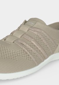 Ανοιχτό μπεζ πλεκτό αθλητικό παπούτσι με ελαστικές λωρίδες πάνω μέρος και λευκή σόλα, σχεδιασμένο για να φοριέται σαν slip-on.