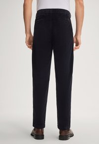 Marineblauwe corduroy broek met rechte snit, zichtbare stiksels en achterzakken met subtiele merktekens.