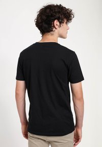 T-shirt nera in cotone con maniche corte e collo rotondo, progettata con una texture liscia e una vestibilità standard, che mostra la vista posteriore.