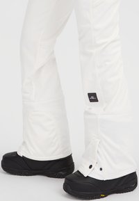 Vita snöbyxor med justerbar mudd, prydda med en logotags och parat med robusta svarta snöskor med strukturerade sulor.
