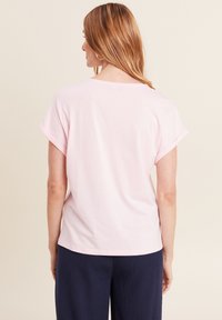 Lichtroze T-shirt met korte mouwen, opgerolde mouwen en een relaxte pasvorm. Van zachte katoen, met een ronde halslijn, gecombineerd met marineblauwe broeken.