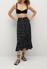 Gonna nera a fiori con orlo svasato, decorata con piccoli fiori blu e bianchi. Abbinata a un top bandeau nero e sandali con lacci.
