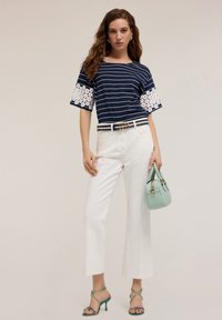 Top de rayas en azul marino y blanco con detalles de ganchillo en forma de flor, combinado con pantalones anchos blancos, tacones verdes con tiras y un bolso menta.