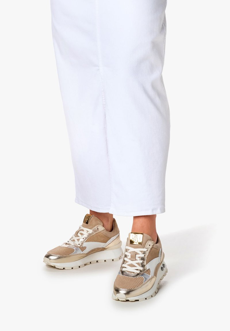 Beżowe i złote buty sportowe z siateczkową teksturą i białymi akcentami. Gruba podeszwa z wzorowanym gripem. Sznurówki i złote detale.