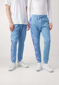 Light blue sweatpants with elastic waistband and cuffs; feature bold blue and white patterned side panels and are paired with white sneakers.
