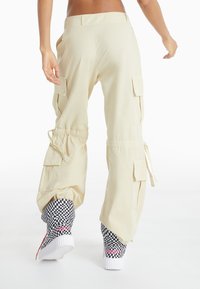 Beige cargo bukser med sidelommer og justerbare manchetter, parret med sort-hvid ternede sneakers med lyserøde accenter.