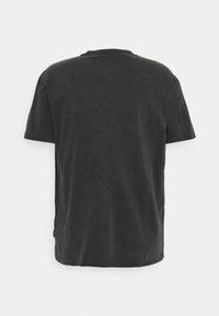 T-shirt noir à manches courtes en coton doux avec un col rond, présentant une coupe décontractée et des détails de bord cousu. Sans graphismes ni motifs.