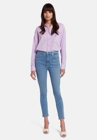 Chemise légère violet clair avec une poche, assortie à un jean slim bleu. La tenue est complétée par des talons beiges à bouts ouverts.