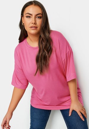 Overmaatse roze gestreepte T-shirt met korte mouwen. Gladde textuur en ronde halslijn, gecombineerd met donkerblauwe aansluitende jeans.