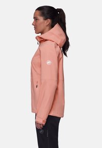 Pfirsichfarbene wasserdichte Jacke mit Kapuze, verfügt über einen Reißverschluss vorne und seitliche Taschen. Logo auf dem linken Ärmel. Glatte Textur.