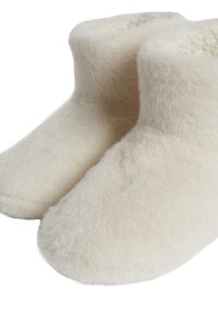 Zapatillas de casa blancas y esponjosas con una textura suave y forma redondeada. Sin hardware visible ni patrones, diseñadas para el calor y la comodidad.