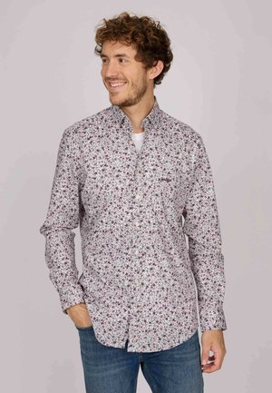 Chemise blanche à bouton avec un motif floral dans des tons de rose et de vert, à manches longues, et un col classique. Portée avec un jean en denim.